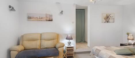 A cozy room with a sofa, a small table with a bowl, a lamp, and a bed with pillows.