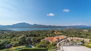 Paisaje costero con vista al mar, montañas y una casa de techo rojo.