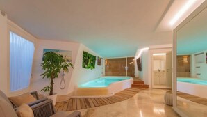 Un interior moderno con una bañera de hidromasaje, suelo de madera, una planta grande y una zona de cocina.
