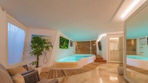 A modern interior with a hot tub, wooden flooring, a large plant, and a kitchen area.