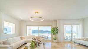 Amplia sala de estar con un sofá grande, una mesa de centro con plantas y vistas al mar a través de amplios ventanales.