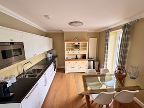 A compact kitchen with modern appliances, a dining area with a glass table, and a view of the outdoors. - Apartment 1 Lochside with Balcony (Onich by Fort William)