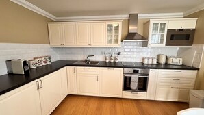 A kitchen with white cabinets, a black countertop, a stove, and a microwave. - Allt Nan Ros Cottage (By Fort William)