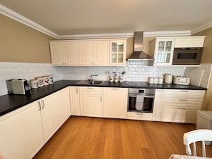 A kitchen with white cabinets, a black countertop, a stove, and a microwave. - Allt Nan Ros Cottage (By Fort William)