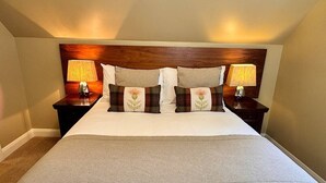 A bedroom with a large bed, two bedside tables with lamps, a headboard, and a carpeted floor. - Allt Nan Ros Cottage (By Fort William)