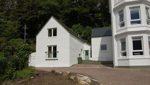 A white building with a gabled roof, a small balcony, and a door with a green frame. - Allt Nan Ros Cottage (By Fort William)