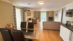 Ein modernes Wohnzimmer mit einem Glastisch, zwei Sofas, einer Küchenzeile mit Mikrowelle und einem Fernseher.