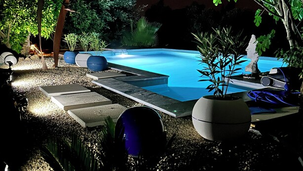 A nighttime outdoor pool area with a stone pathway, potted plants, and a well-lit pool. - Bed and breakfast in the south of France (Entre-Vignes)