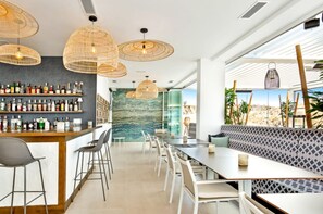 A modern bar area with a variety of liquor bottles, wicker pendant lights, and a seating area with patterned cushions. - La Calma | Terrace - pool - gym (Mijas)
