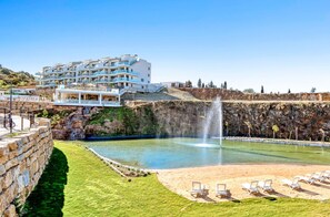 A pool with a fountain, sun loungers, and a building with multiple balconies. - La Calma | Terrace - pool - gym (Mijas)