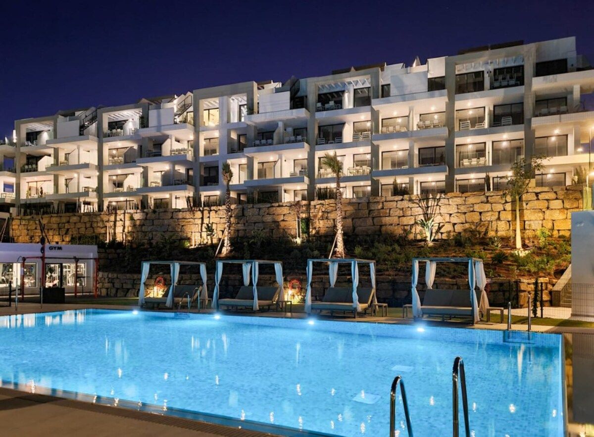 A multi-story hotel with a swimming pool, outdoor seating, and a stone wall backdrop.