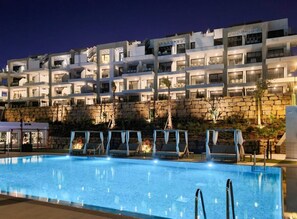 A multi-story hotel with a swimming pool, outdoor seating, and a stone wall backdrop. - La Calma | Pool - Gym - Terrace (Mijas)