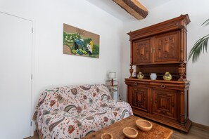 A living room with a patterned sofa, a wooden cabinet, and a painting on the wall. - Charming 1-Bedroom Apartment with Garden in the Heart of the Countryside (Sainte-Marie-de-Gosse)