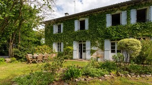 A two-story house with ivy-covered walls, a stone pathway, and a dining area with outdoor furniture. - Charming 3-Star Home Between Landes and Basque Country (Sainte-Marie-de-Gosse)