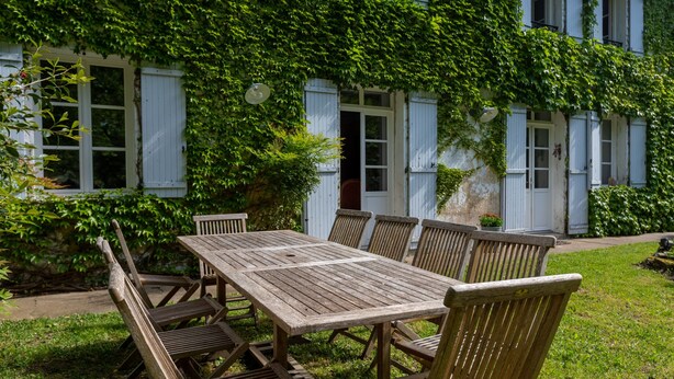 A wooden table and chairs set outside a building with white shutters and green ivy. - Charming 3-Star Home Between Landes and Basque Country (Sainte-Marie-de-Gosse)