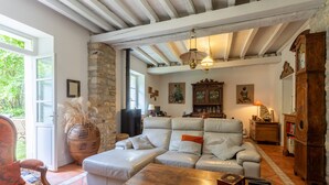 A cozy living room with a stone wall, a leather sofa, a wooden coffee table, and a large window. - Charming 3-Star Home Between Landes and Basque Country (Sainte-Marie-de-Gosse)