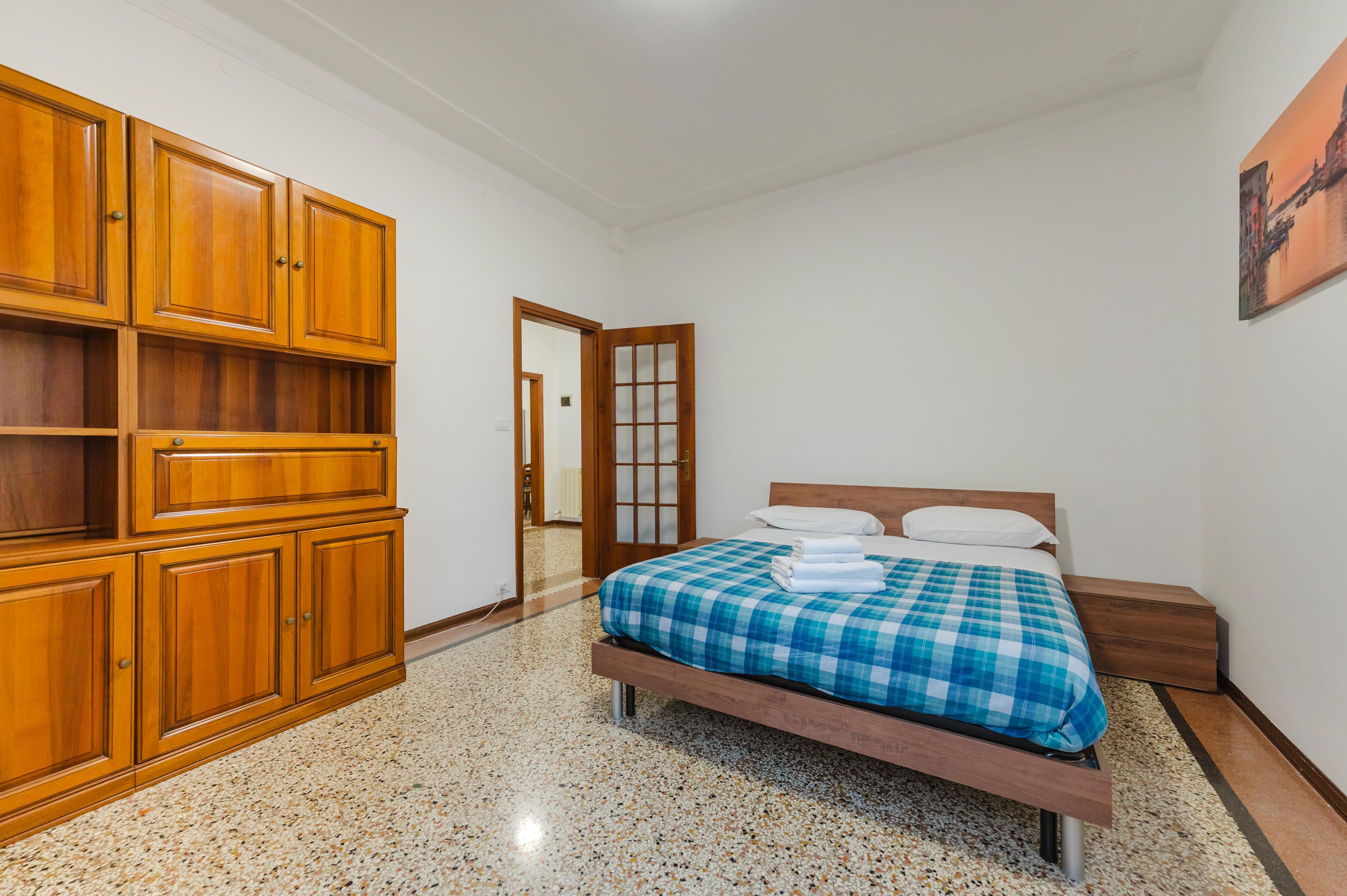 A bedroom with a bed, wooden wardrobe, and a door leading to another room.