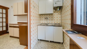 A compact kitchen with white cabinets, a built-in oven, and a window with a view. - Casa Tatiana (Mestre)