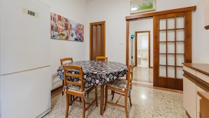 A dining area with a round table, four chairs, a refrigerator, a painting, a wooden door, and a cabinet. - Casa Tatiana (Mestre)