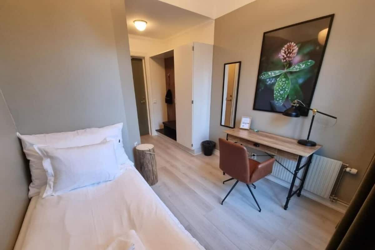 Une chambre d’hôtel avec un lit, un bureau, une chaise, un miroir et un tableau encadré au mur.