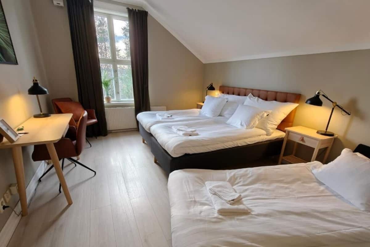 Une chambre d’hôtel avec deux lits, un bureau, une chaise et une fenêtre avec des rideaux.