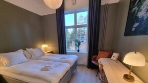 A bedroom with a double bed, a small table, a chair, a window with curtains, and a potted plant. - Norrkällan (Vännäs)