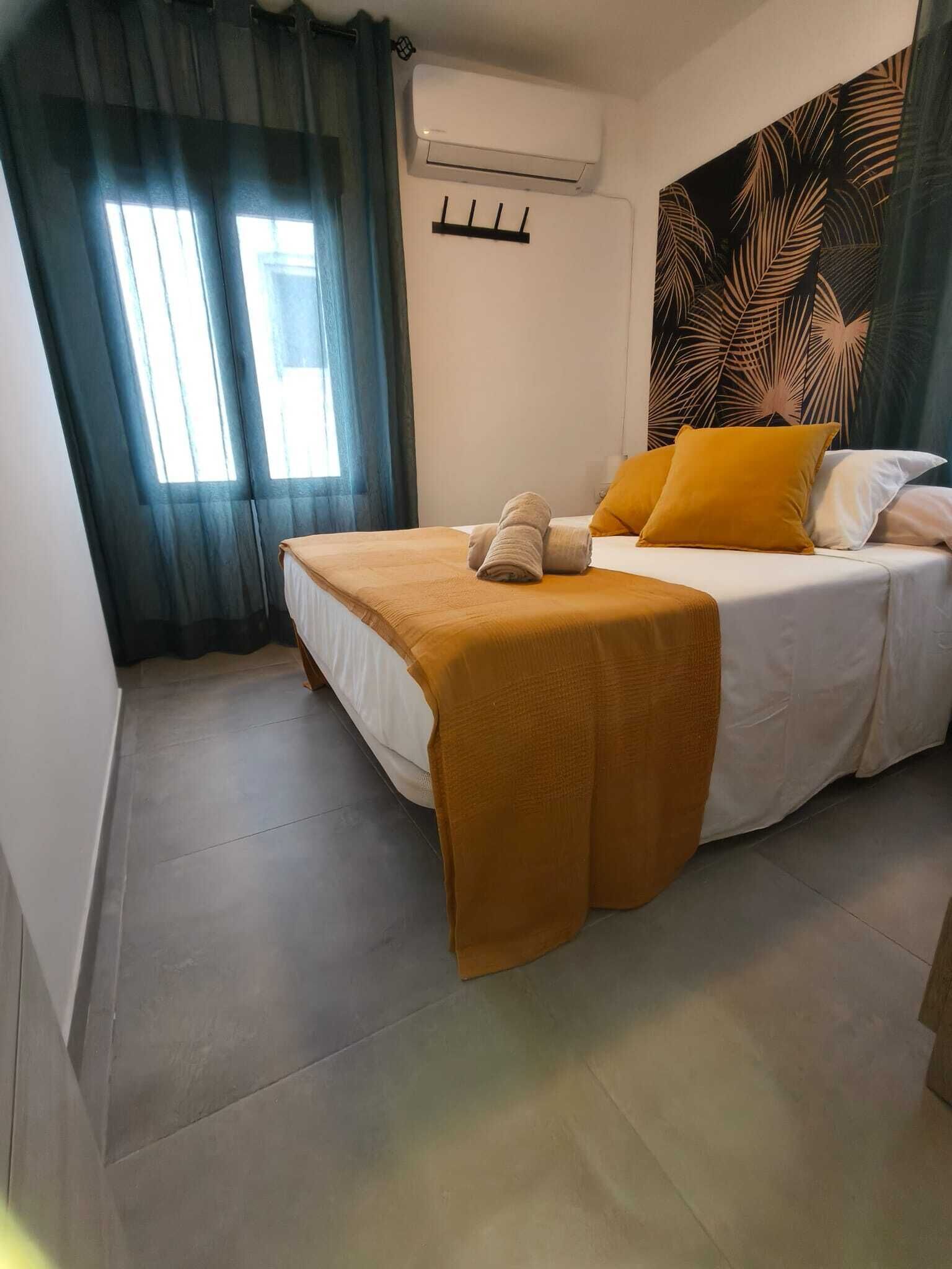 A bedroom with a bed, a towel, a wall-mounted air conditioner, and a large leaf-patterned tapestry.