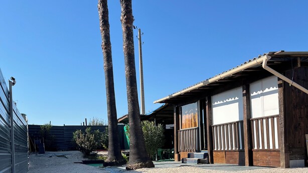 Un bâtiment avec une allée en gravier, une structure en bois et un ciel d’un bleu éclatant.