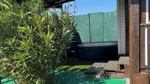 Un espace extérieur abrité, doté d’une pelouse artificielle verte, d’un petit jardin avec des fleurs blanches et d’une terrasse en bois.