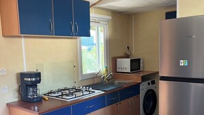 Une cuisine compacte équipée d’une cuisinière à gaz, d’un four à micro-ondes, d’un lave-linge et d’un réfrigérateur.
