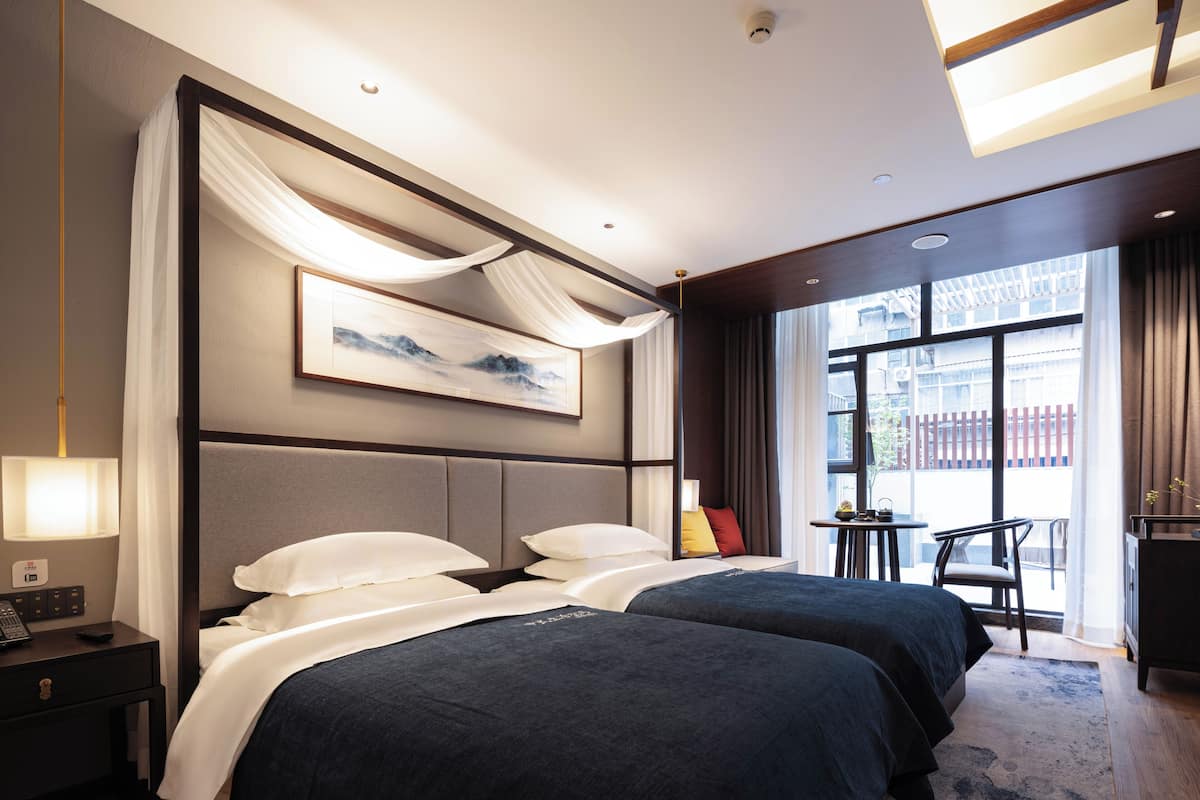 A hotel room with two beds, a desk, a chair, and a large window.