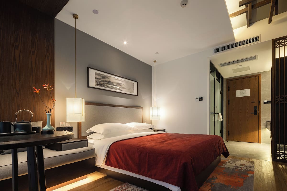A modern hotel room with a bed, bedside table, lamp, and a framed picture on the wall.