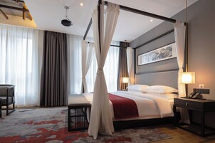 Ein Hotelzimmer mit Bett, Nachttisch, Lampe und Blick ins Freie.