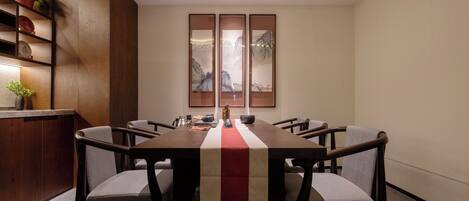 Un salón de conferencias con una larga mesa, seis sillas, un camino de mesa rojo y blanco, y obras de arte enmarcadas en la pared.