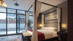 Una habitación de hotel moderna con un ventanal grande, una cama con dosel, una mesita de noche y otro mueble auxiliar.
