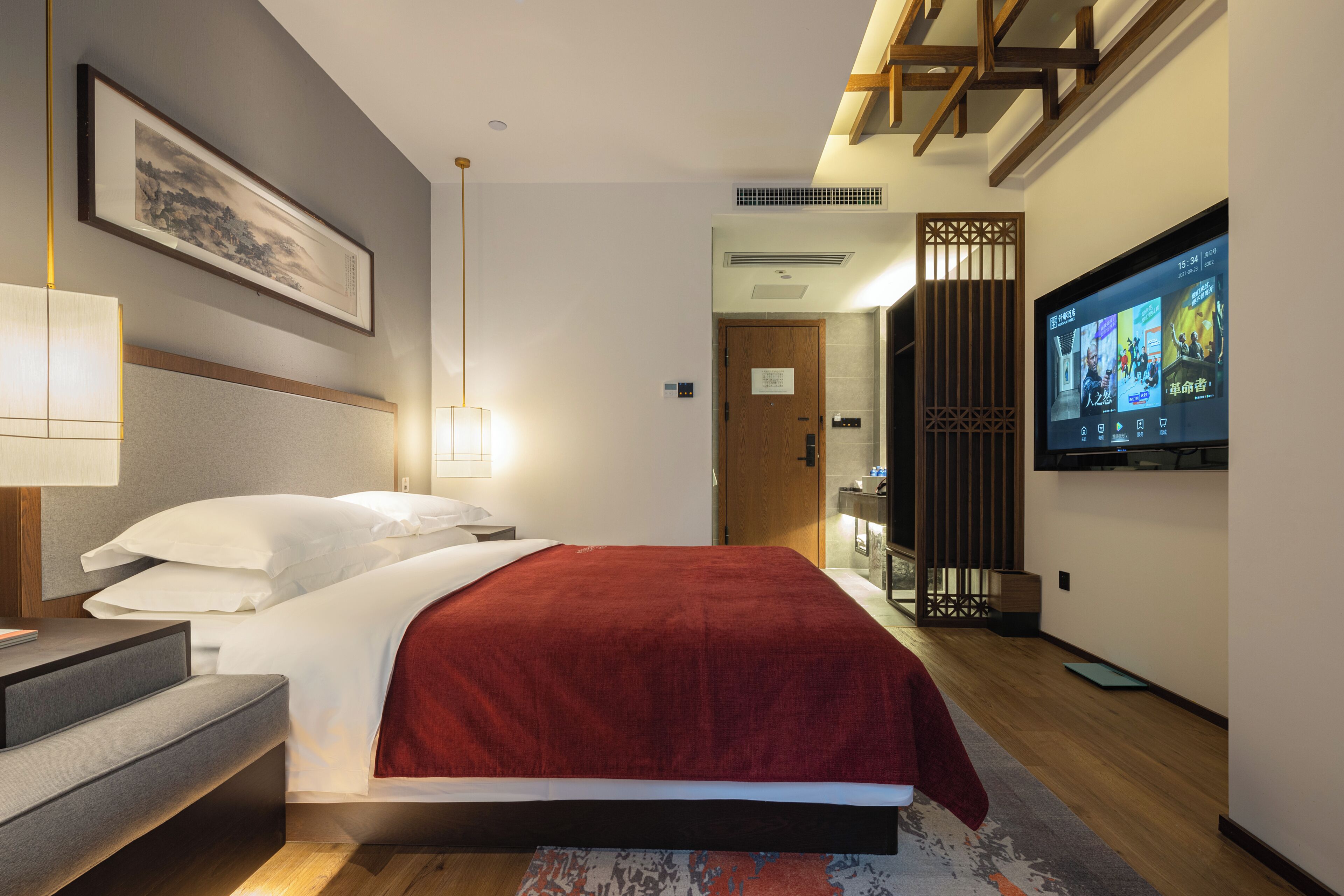 Une chambre d’hôtel moderne équipée d’un lit, d’une table de chevet, d’une lampe, d’une télévision et donnant sur le couloir.
