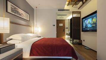 A modern hotel room with a bed, bedside table, lamp, TV, and a view of the hallway.
