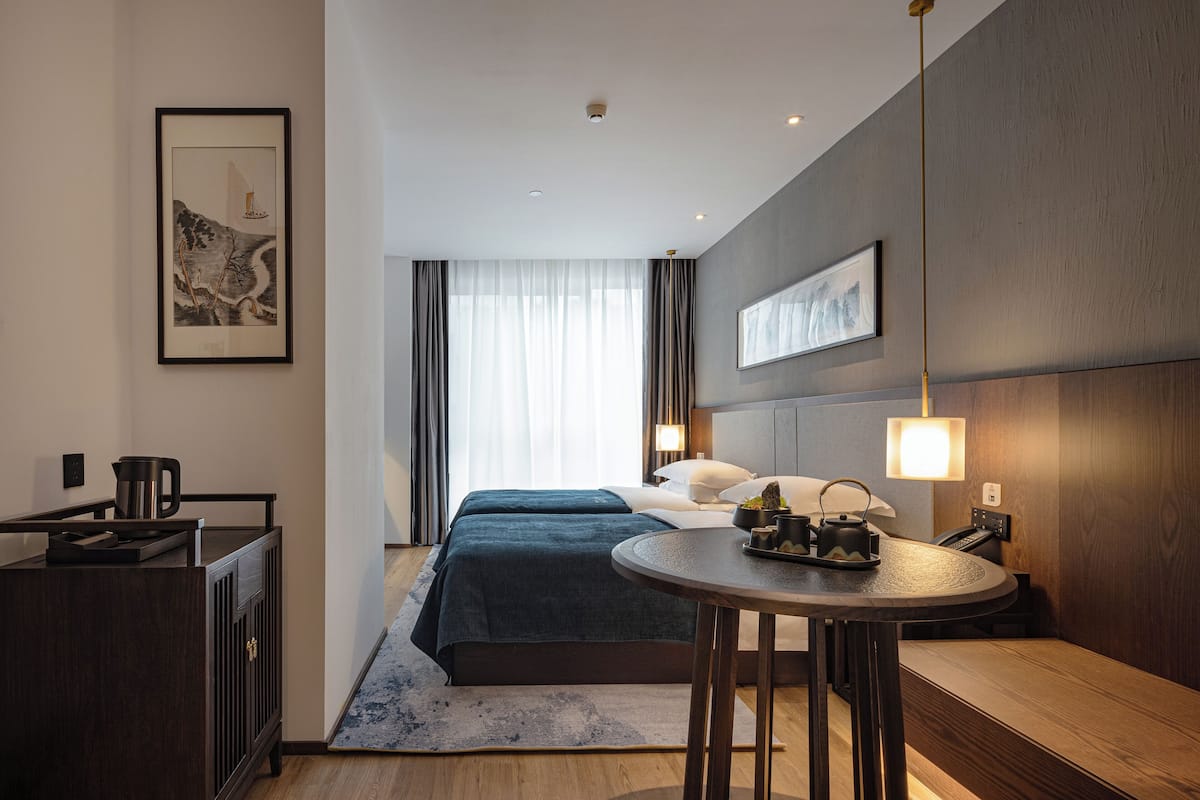 A hotel room with a bed, bedside table, lamp, and artwork on the walls.
