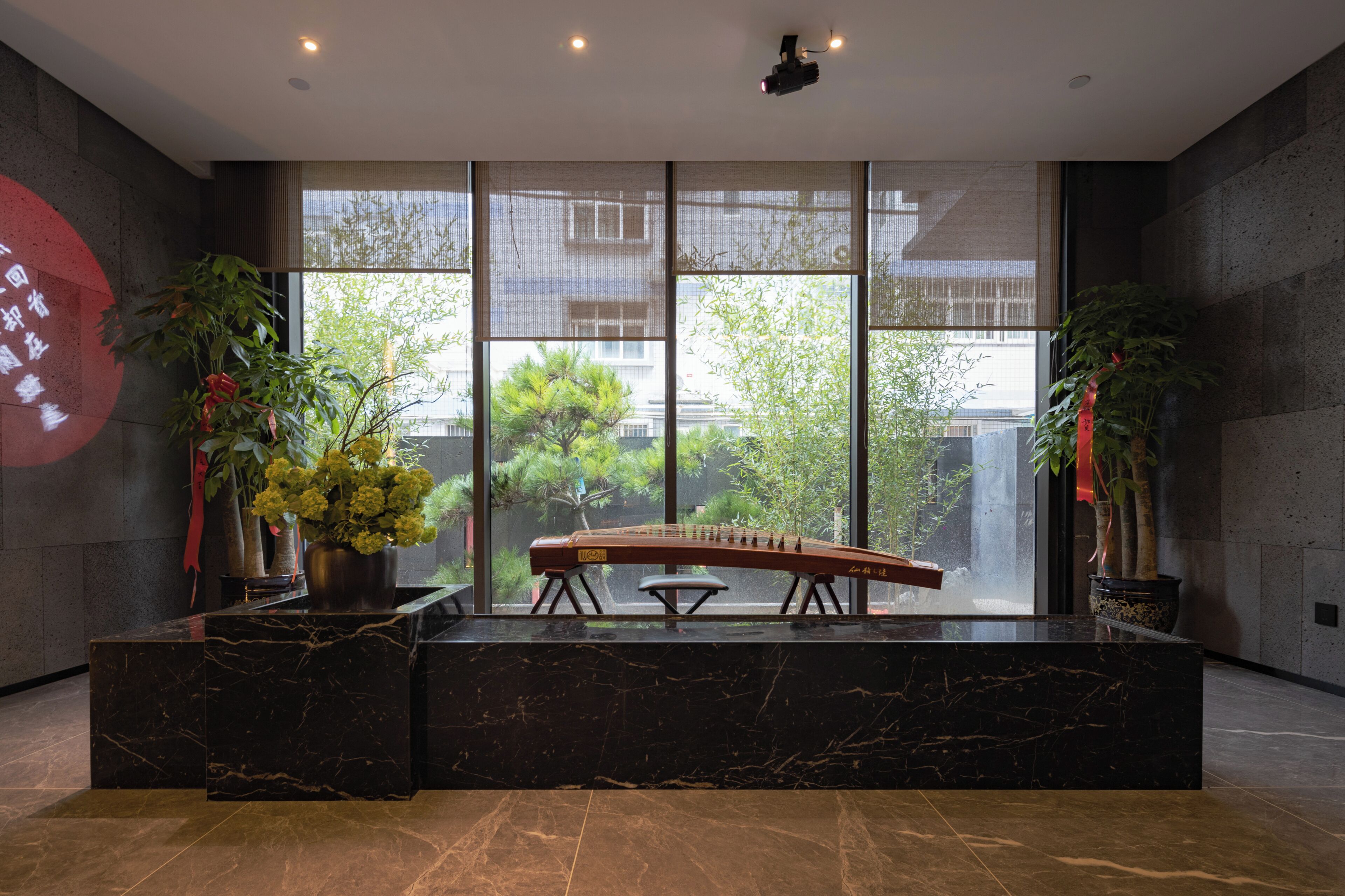 A reception area with a marble counter, potted plants, a traditional stringed instrument, and large windows offering a view of greenery and buildings.