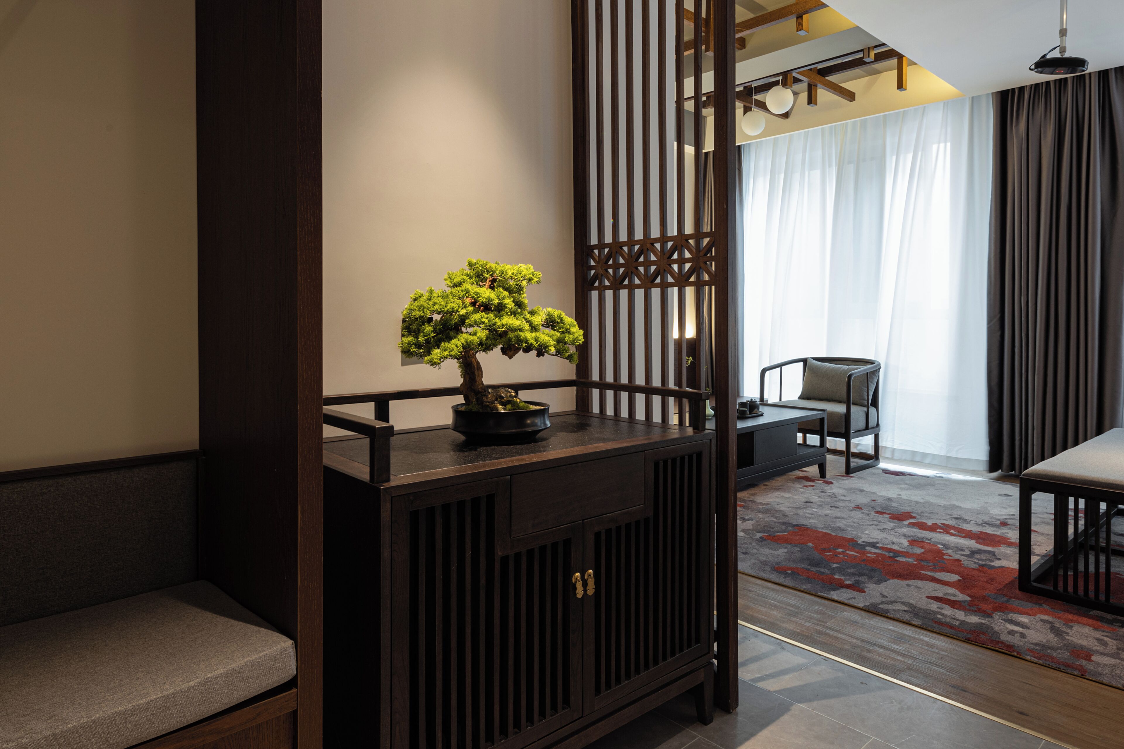 Een kamer in traditionele stijl met een houten console tafel, een bankje, een bonsai in pot en een schuifdeur.