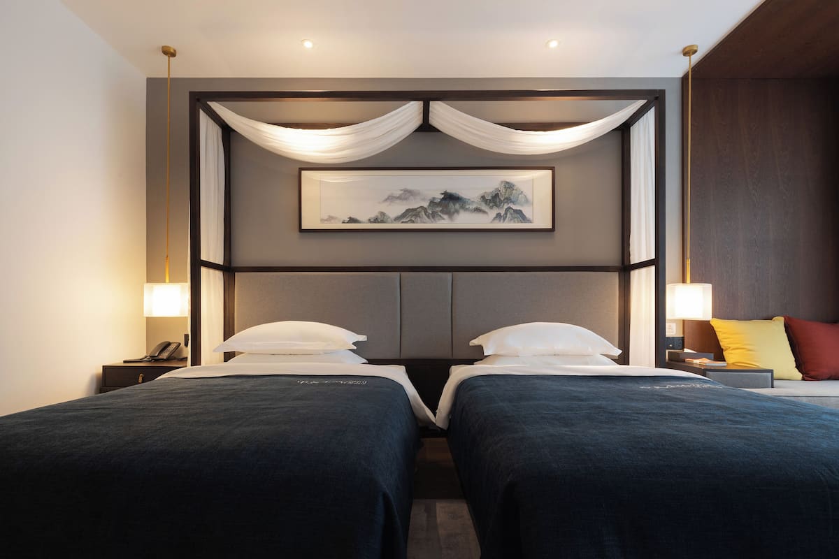 A hotel room with two beds, a framed artwork on the wall, and bedside lamps.