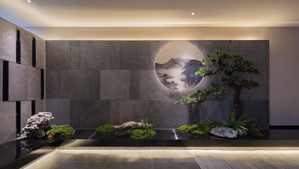 Un interior moderno con pared de piedra, un espejo circular y una fuente de agua minimalista.
