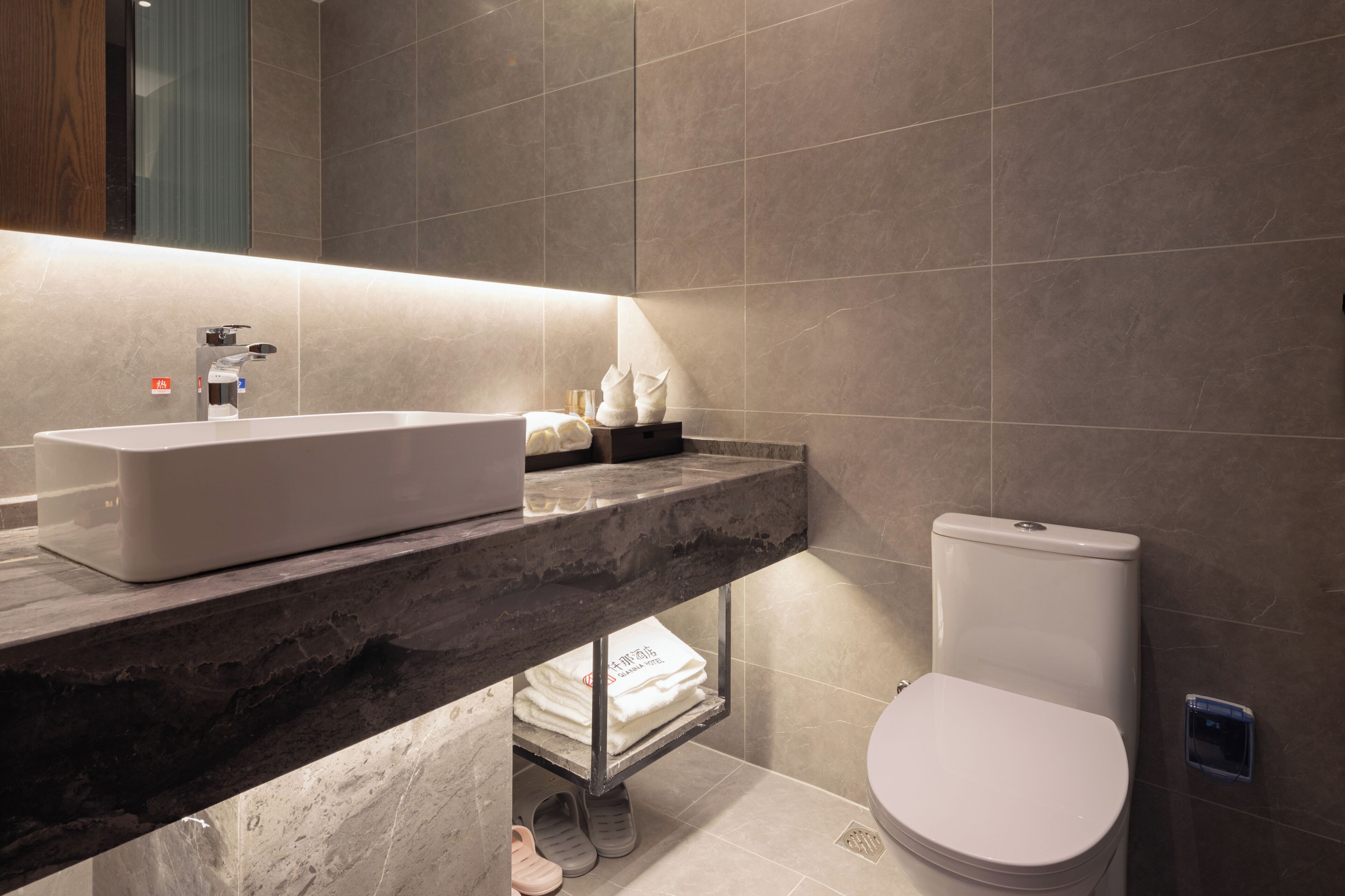 Un baño moderno con encimera de mármol, un lavabo blanco y un inodoro.
