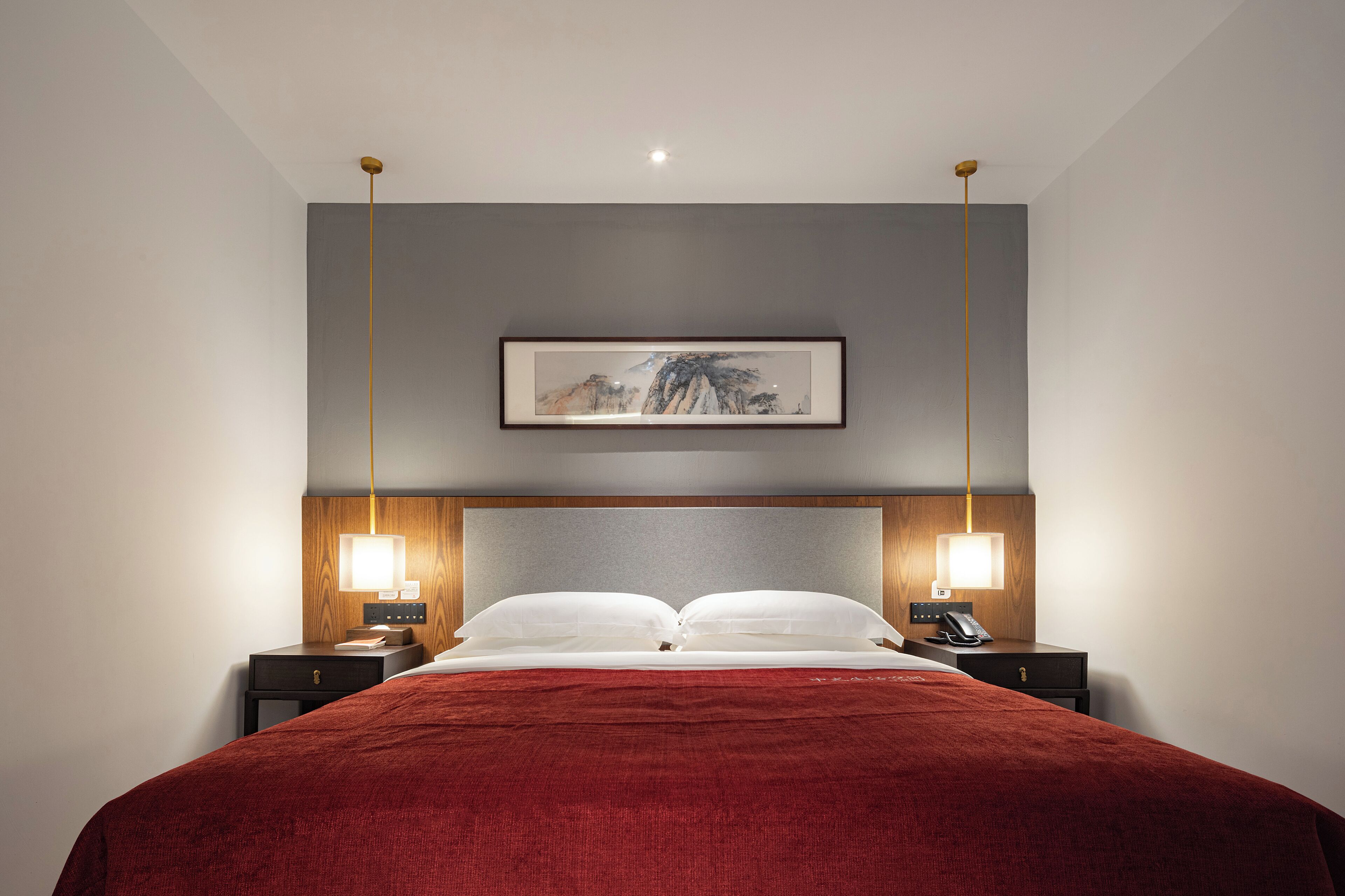 A hotel room with a large bed, two bedside tables, a nightstand, a framed artwork on the wall, and a ceiling light fixture.