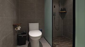 A modern bathroom with a toilet, a trash bin, a shower area, and a shelf with toiletries.
