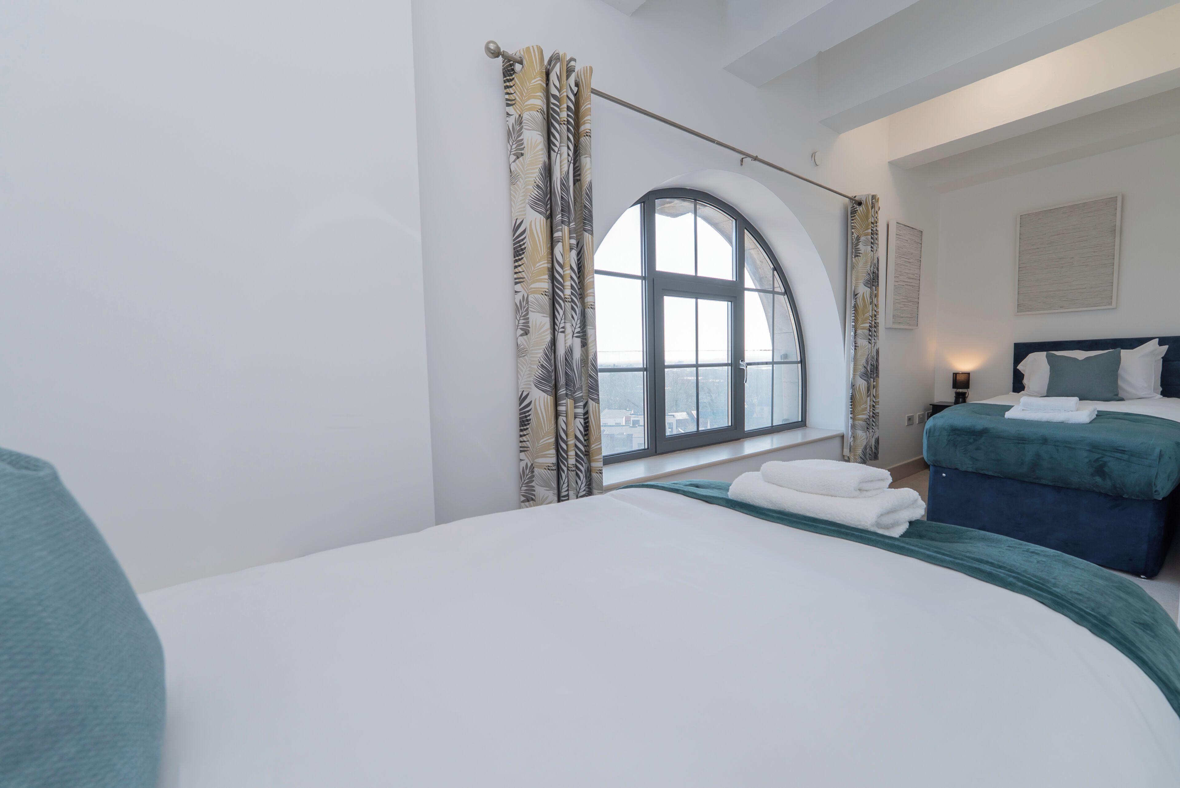 A hotel room with a large arched window, two beds, and a view of the city.