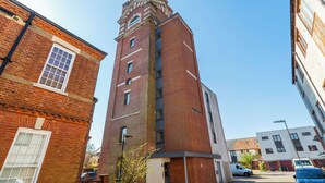 A tall brick building with a clock tower, adjacent to a white building with a flat roof.