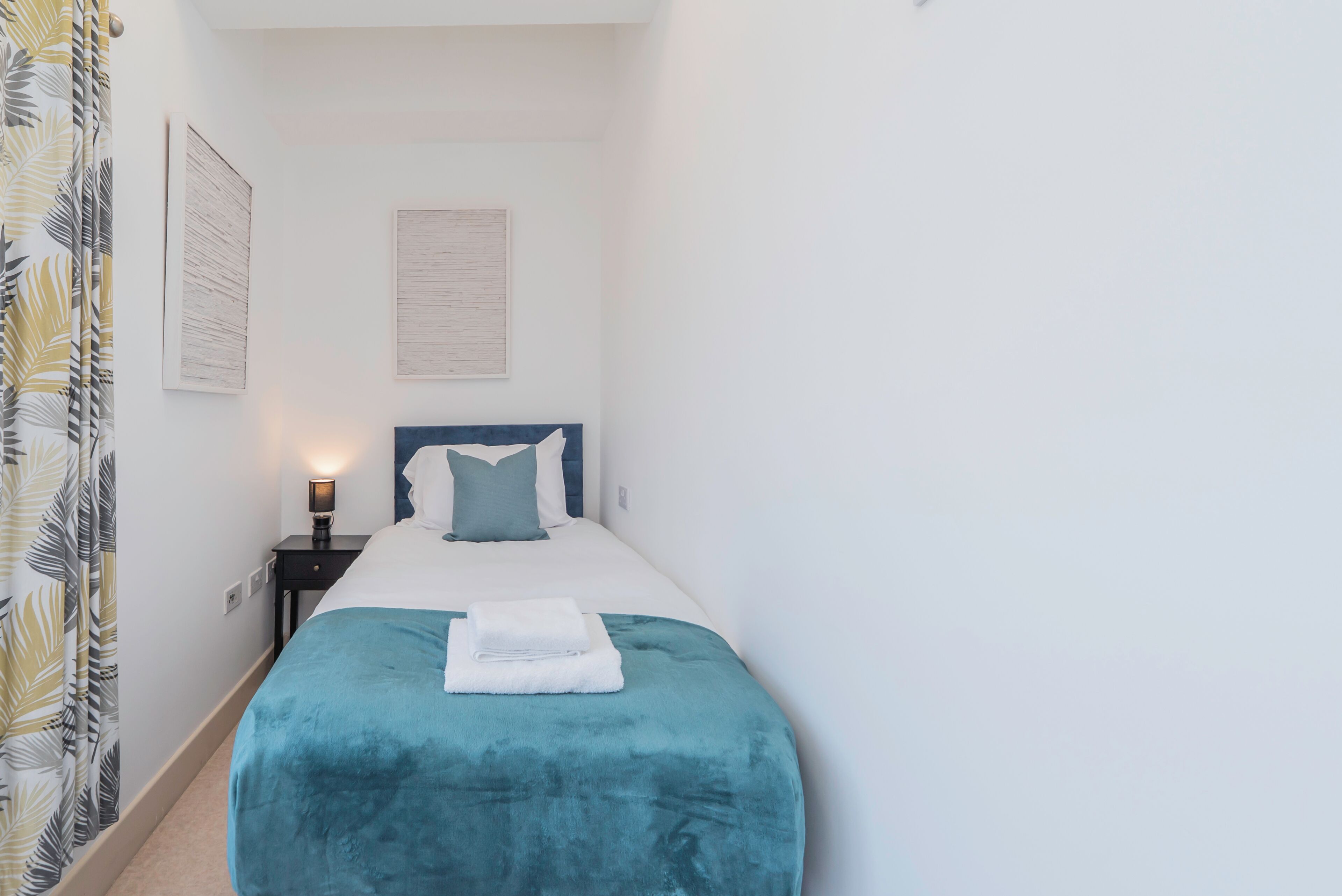 A bedroom with a bed, a nightstand, a lamp, and a curtain.