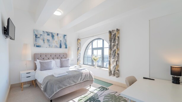 A bedroom with a bed, bedside table, lamp, and a large window with curtains.