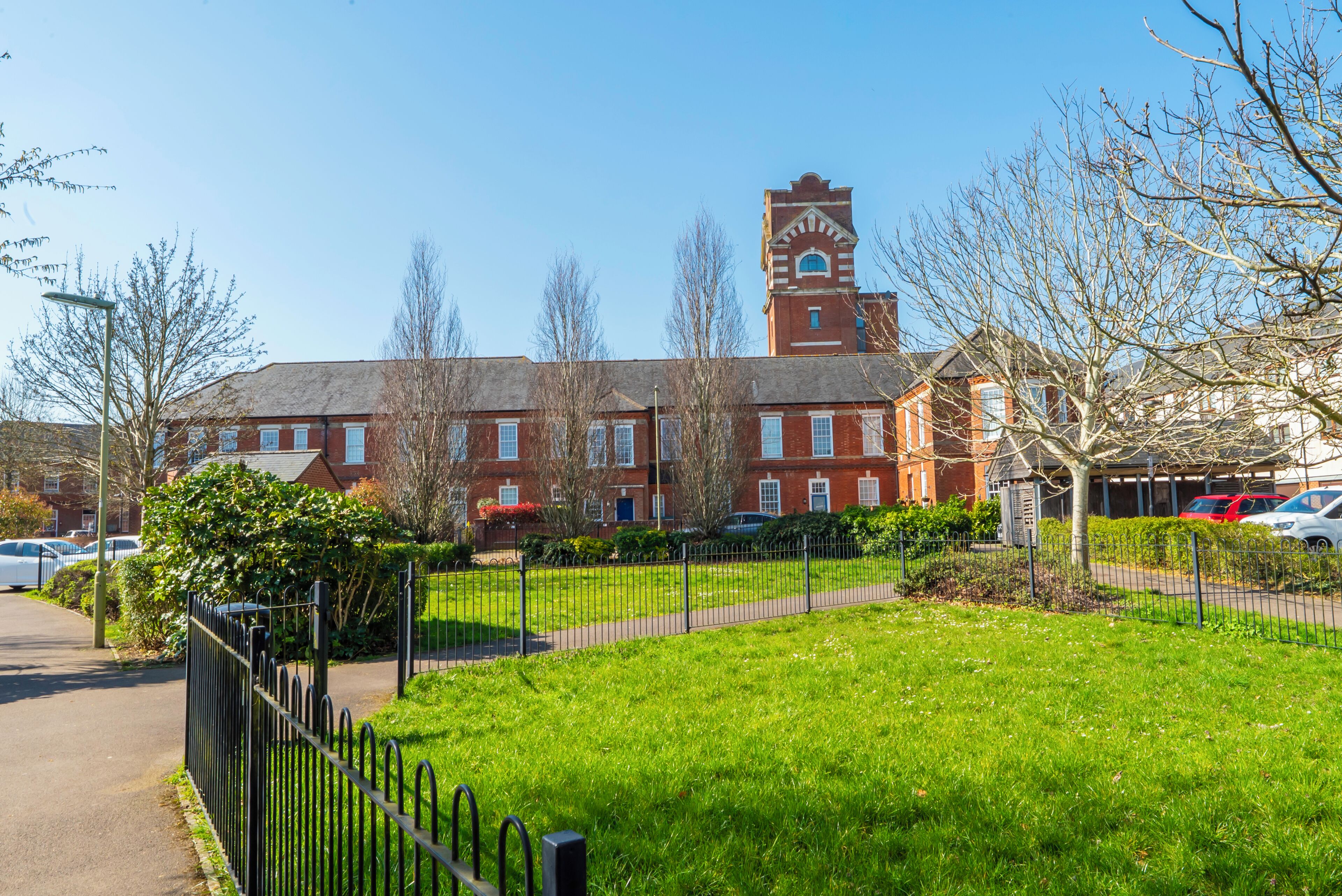 A red brick building with a clock tower, surrounded by a green lawn and a black fence.
